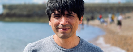 A man with dark hair stood in front of a beach. 