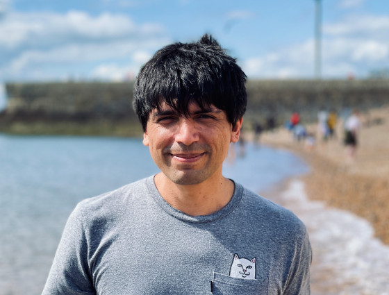A man with dark hair stood in front of a beach. 